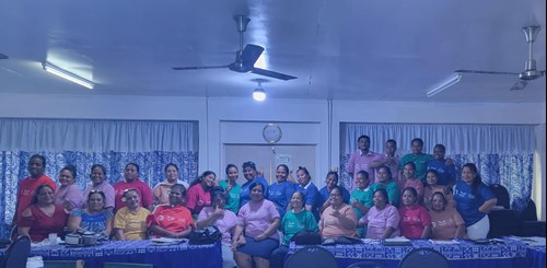 31 people post for a photo in an office in Kiribati. They are all wearing matching T-shirts of various colours. There are three rows: 11 sitting in the front; 18 standing behind; and 4 are standing tall to the right.