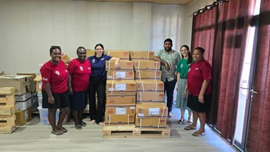 A group of 5 women and 1 man stand around a large amount of cardboard boxes in an office space