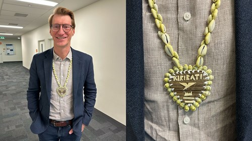 There are two photos next to each other. The first photo is of Professor Andrew Steer who is wearing glasses and a shell necklace. The second photo is a close up of the shell necklace. It has a shell chain with a large pendant in the shape of a love heart and Kiribati written on it with a picture of a bird.