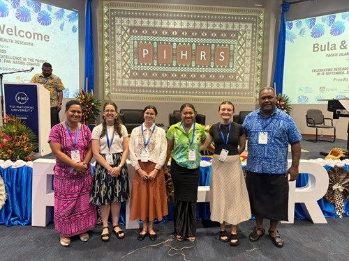 5 women stand with 1 man (on the far right), in front of the PIHRS stage in full view. They are standing side by side and smiling at the camera.